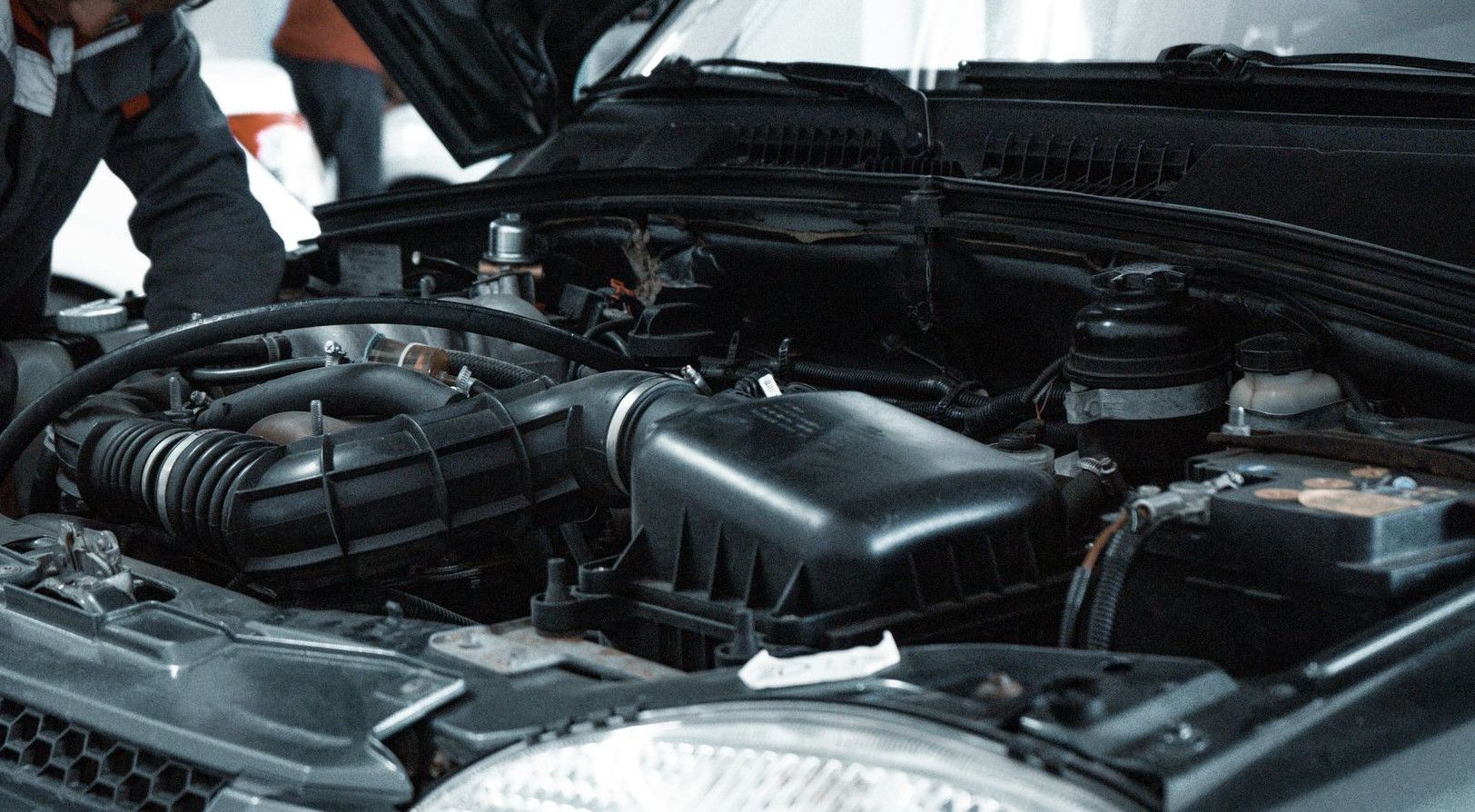 A mechanic in a grey uniform inspecting the engine of a car